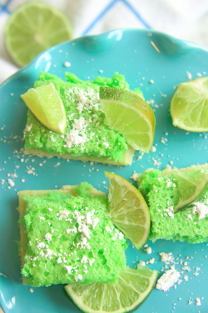 vertical close up of green gluten-free lime bars on a blue platter with powdered sugar and lime slices