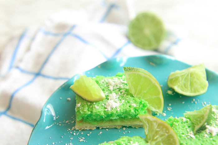 close up green gluten-free lime bars on a blue platter with powdered sugar and lime slices