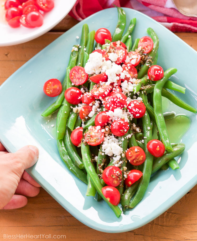 These 5 minute greek green beans use fresh cooked green beans that are drizzled with a quick homemade greek dressing and topped with fresh tomato and feta cheese crumbles. They are great served warm or cold and are perfect for all those summer parties!