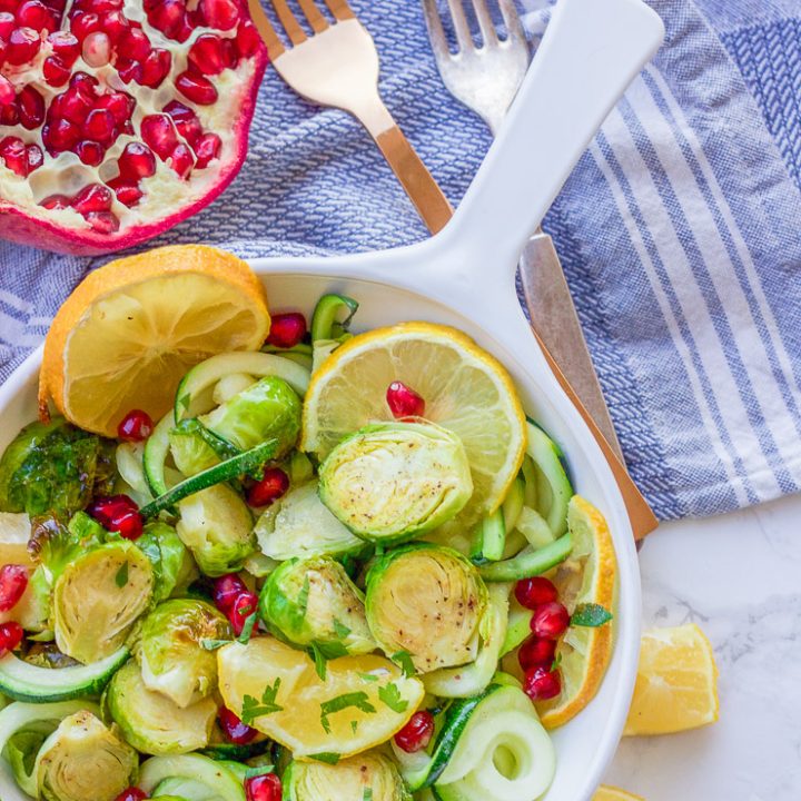 This roasted lemon garlic brussel sprouts + zucchini recipe is a clean, crisp, savory vegetable dish that is not only healthy but a gorgeous and easy addition to any meal! Lemon, honey, and garlic flavors coat the roasted brussel sprouts, zucchini noodles, and pomegranate arils for a colorful fresh salad.