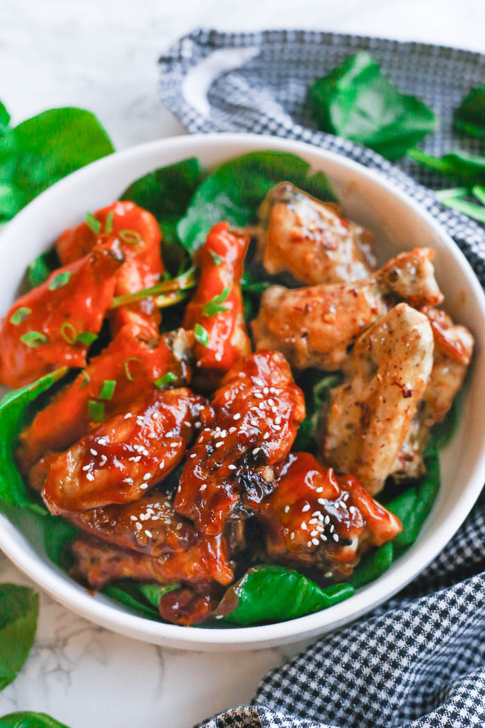air fryer chicken wings with three different sauces in white bowl with vegetable greens