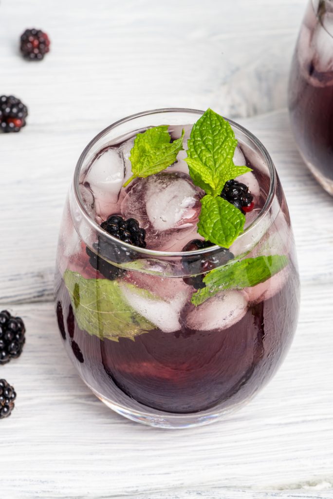 a glass containing blackberry purple haze cocktail with raw berries & mint leaves