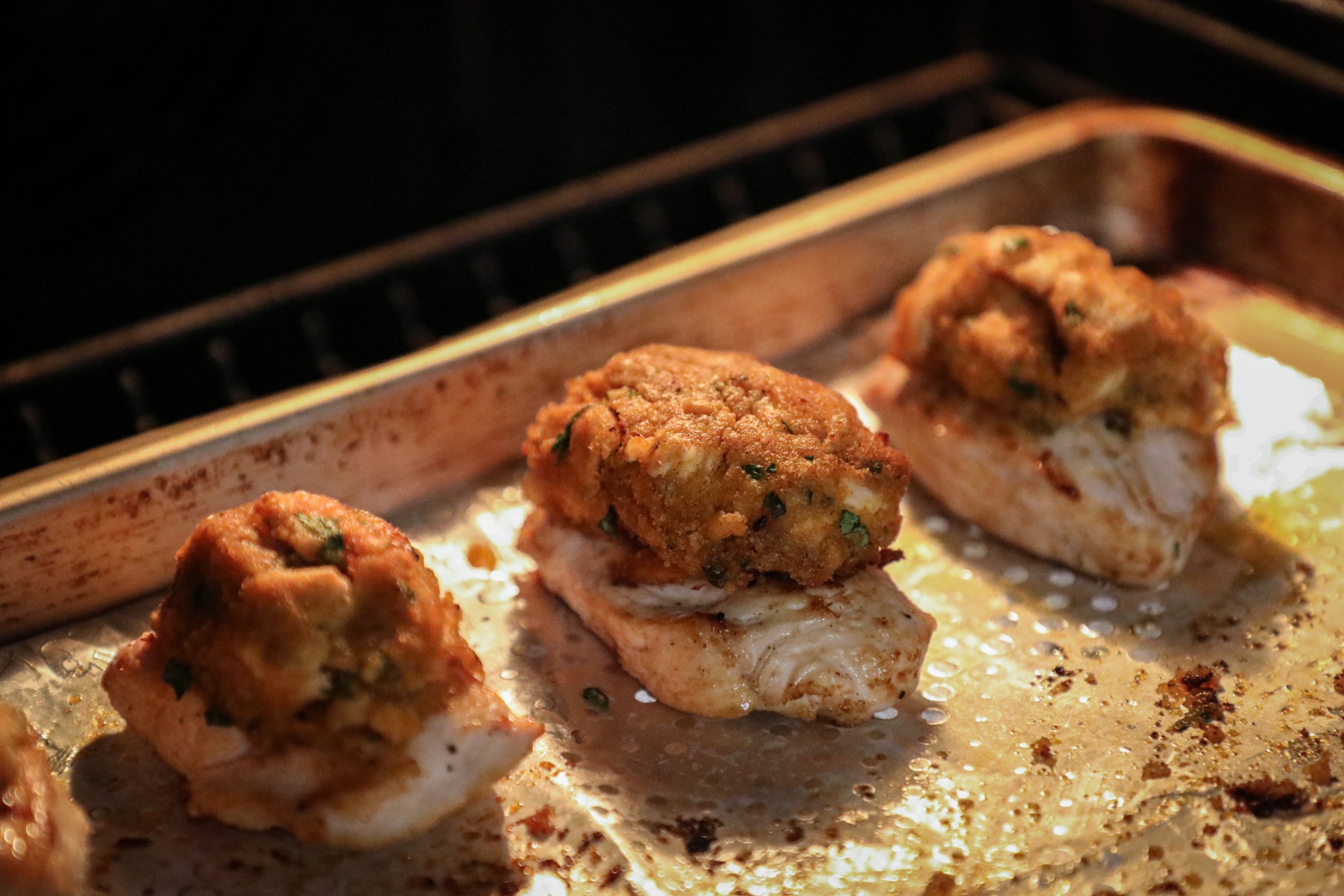 3 chicken breasts with crab mix ball on top, cooking in the oven