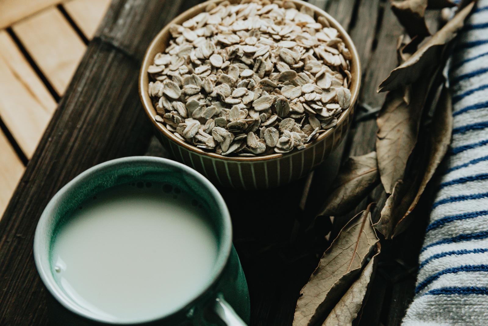 A breakfast of a cup of oat milk with oat seeds over a wooden plank