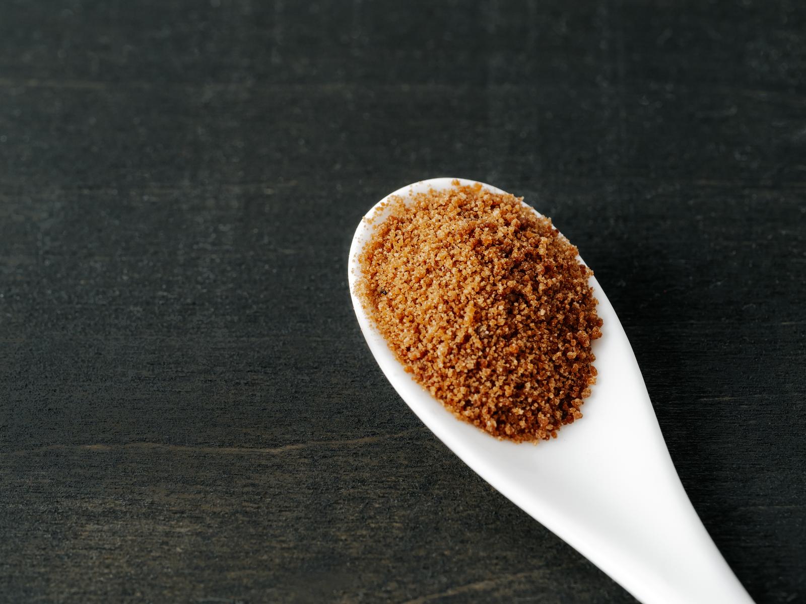 Spoon of coconut brown sugar on dark wooden background.
