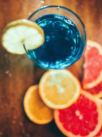 A glass of blue curacao coktail and agrums displayed on a wooden plank